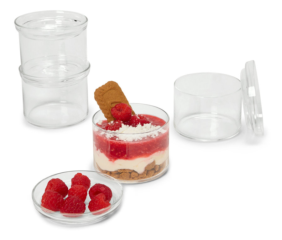 Quatre verres à apéritifs et à desserts et un dessert aux framboises avec un biscuit sur fond blanc.