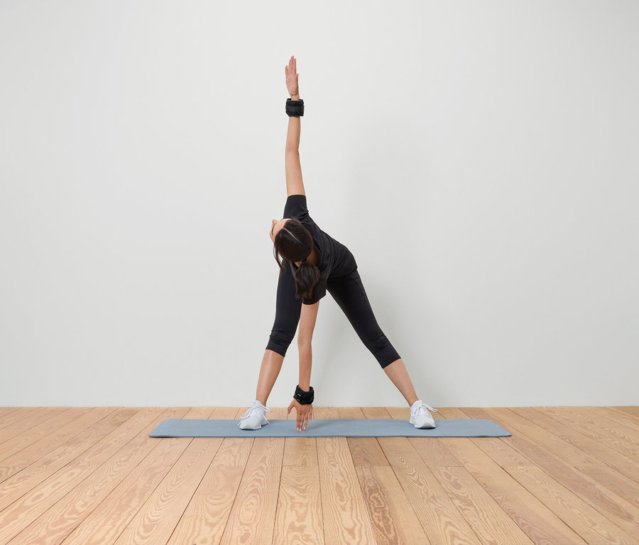 Femme faisant des étirements sur un tapis avec des poids aux poignets et aux chevilles.
