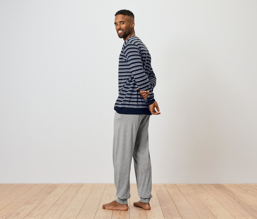 Un homme regarde par-dessus son épaule et sourit. Il porte un haut rayé et un pantalon de jogging gris.