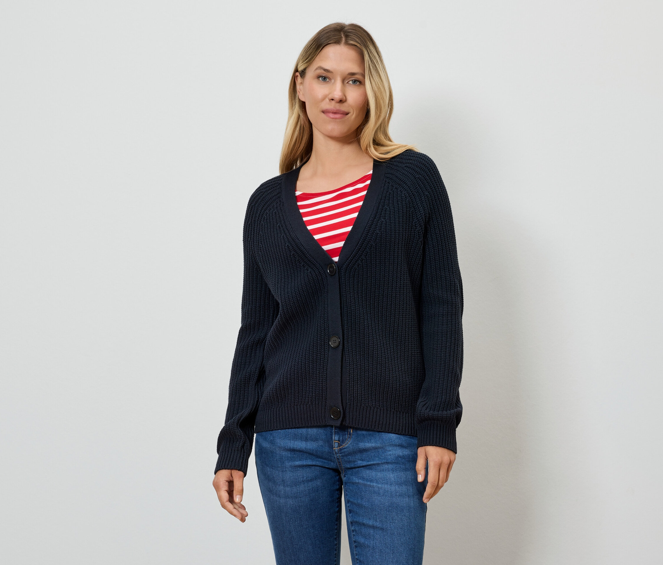 Une femme porte un cardigan bleu marine sur un t-shirt rayé rouge et blanc et un jean.
