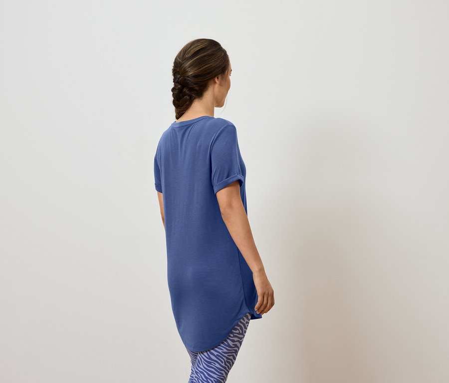 Une femme portant un t-shirt bleu et des leggings à motifs, vue de dos.