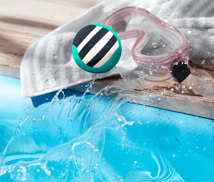 Ballon rebondissant pour l’eau atterrissant dans une piscine à côté d’une serviette et de lunettes de protection.