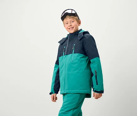 Un garçon portant une veste et un pantalon de ski, avec des lunettes de ski sur la tête.