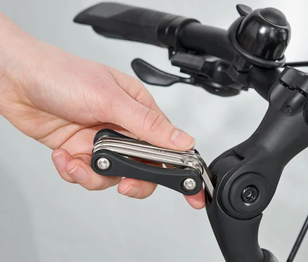 Une main utilise un outil multifonction sur le guidon d'un vélo.