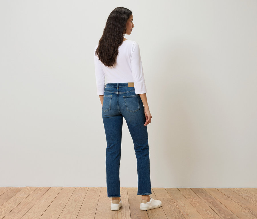 Une femme, vue de dos, porte un jean bleu, un t-shirt blanc et des baskets blanches.