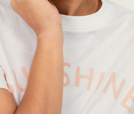 Femme souriante touchant son visage, portant un t-shirt à imprimé.