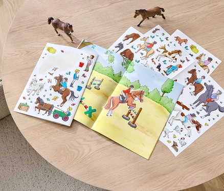 Un livre d'autocollants « Chevaux et poneys » ouvert sur une table, à côté de deux figurines de chevaux.