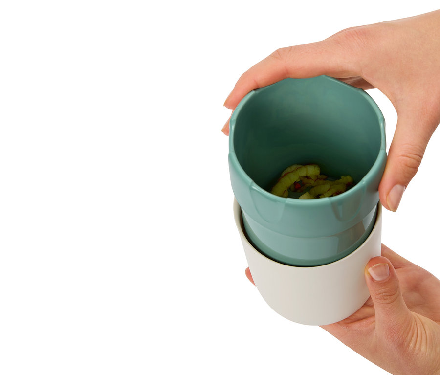 Les mains tiennent deux tasses, celle du dessus est turquoise avec un contenu, celle du dessous est blanche.