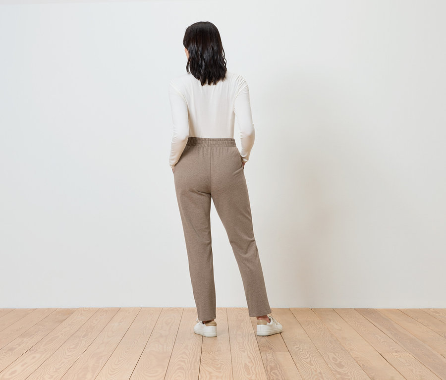 Une femme, vue de dos, porte un pantalon marron et un haut blanc.