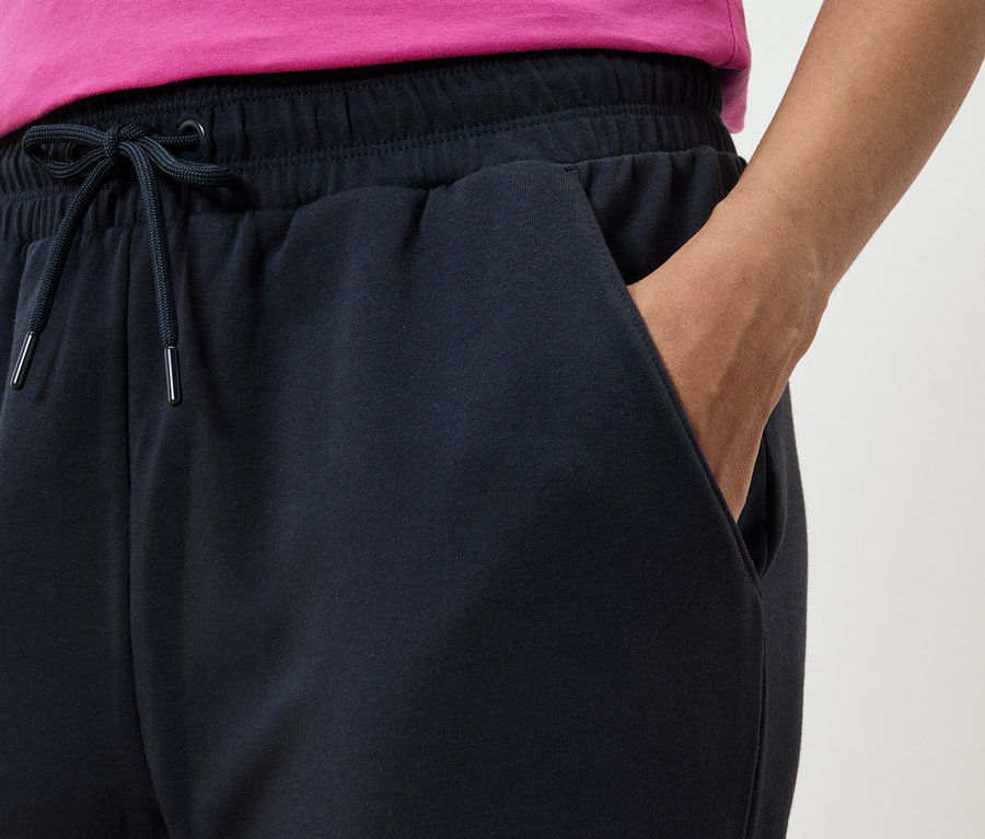 Gros plan d'un pantalon de survêtement bleu marine avec une main dans la poche et un t-shirt rose.