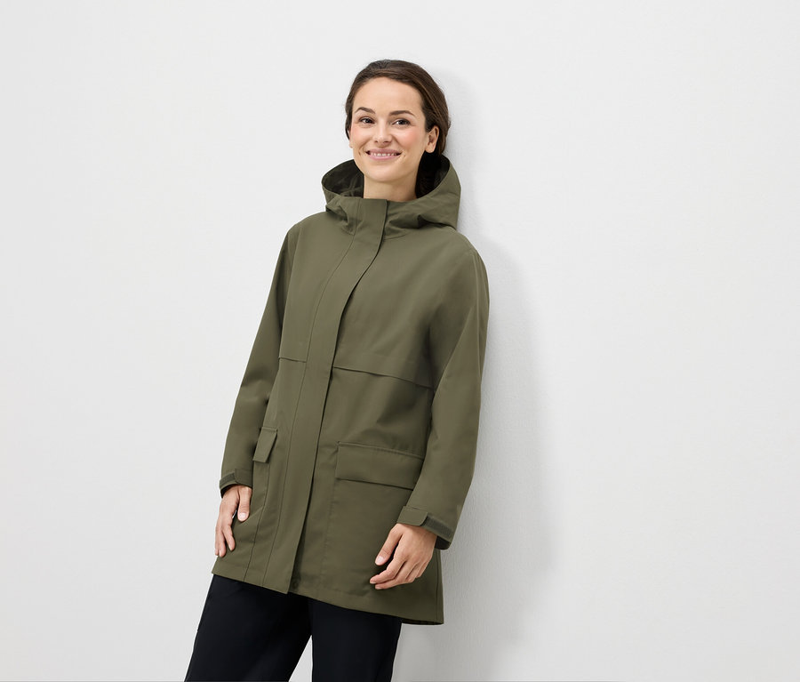 Femme posant en veste à capuche vert olive et pantalon noir.