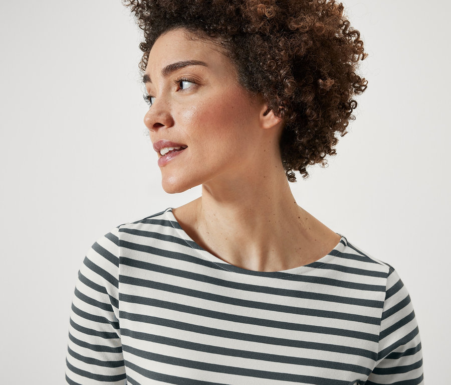 Portrait d'une femme aux cheveux courts et bouclés. Elle porte un t-shirt à rayures vertes à manches courtes.
