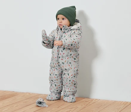 Bébé portant une combinaison de neige à motifs floraux et un bonnet vert.