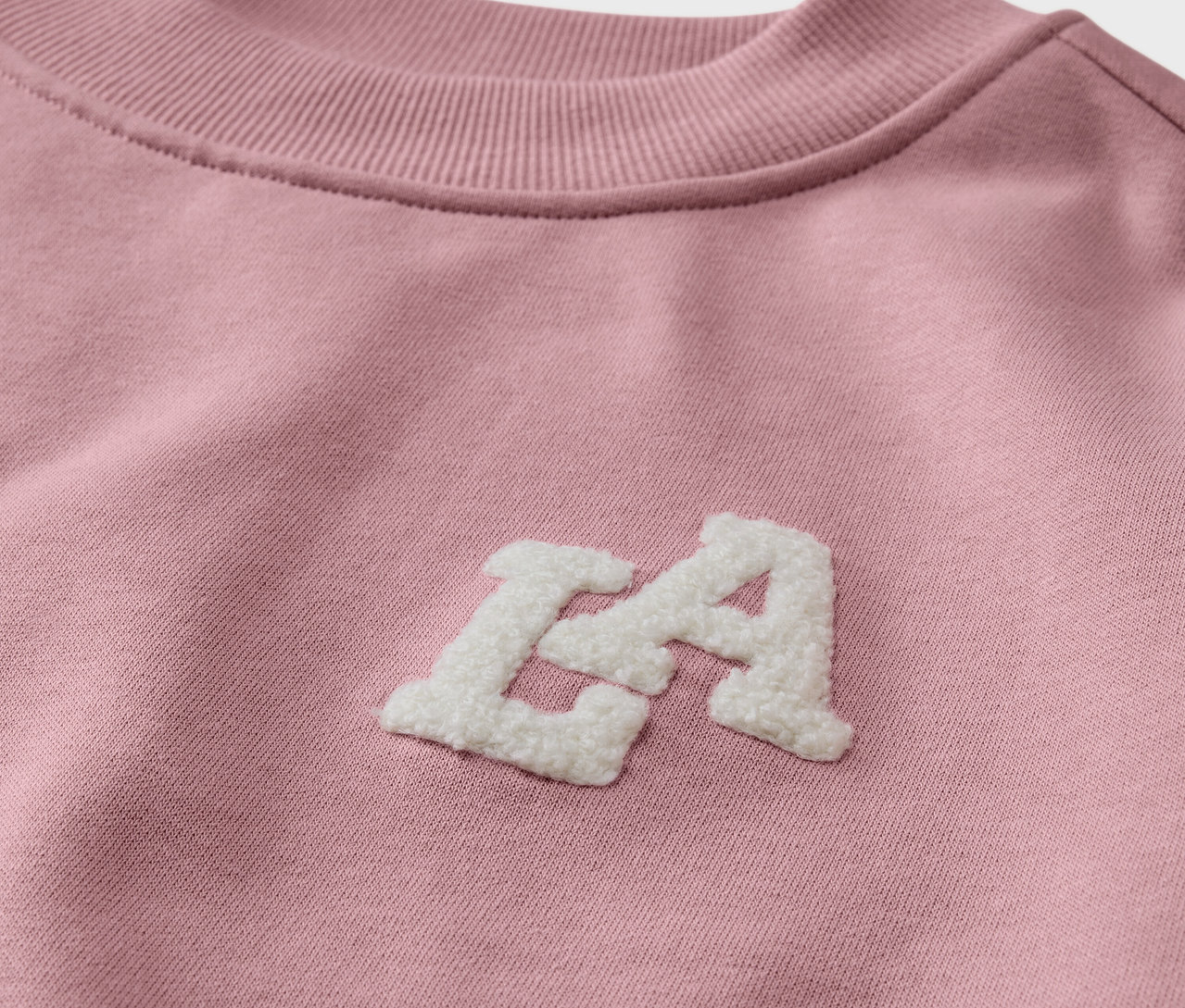 Gros plan sur un sweatshirt rose pour enfant avec intérieur gratté et inscription blanche "LA".