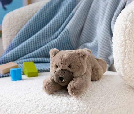 Un ours en peluche marron est allongé sur un fauteuil blanc et moelleux à côté de blocs de bois.