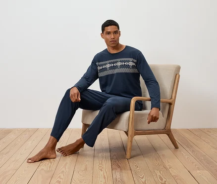 Un homme est assis dans un fauteuil et porte un pyjama bleu marine à manches longues avec un motif.