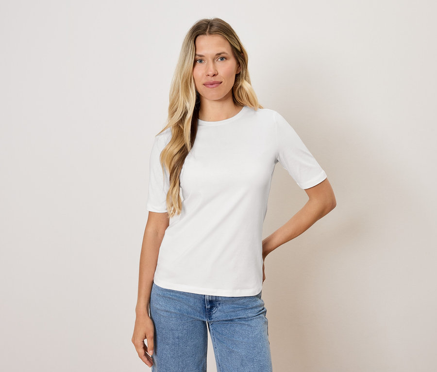 Femme blonde posant dans un t-shirt blanc et un jean bleu.