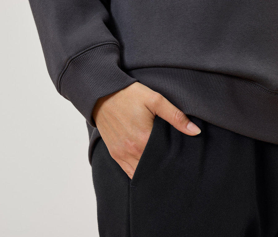 Gros plan d'une femme, la main dans la poche d'un pantalon de survêtement noir, portant un sweat-shirt gris.
