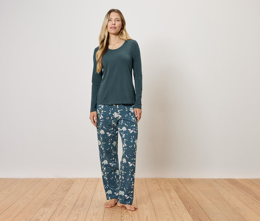 Une femme debout porte un pyjama vert foncé à manches longues et un pantalon à fleurs.