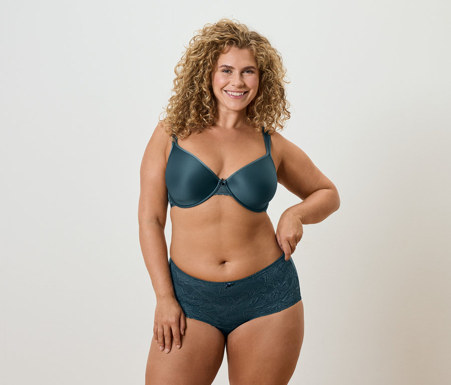 Femme aux cheveux blonds bouclés portant un soutien-gorge pétrole et des sous-vêtements assortis.