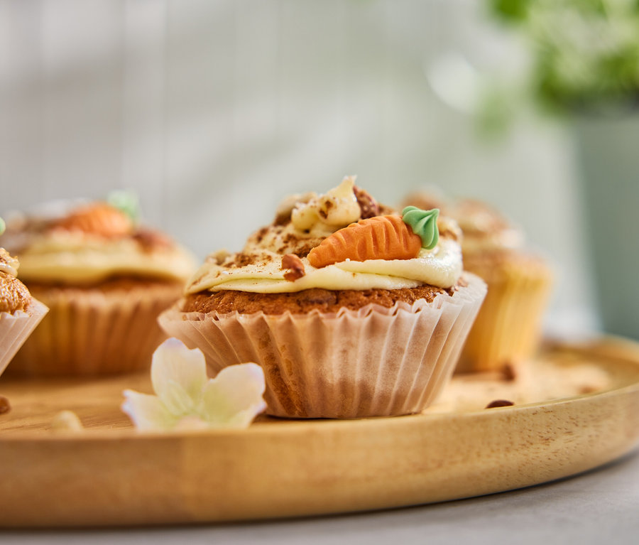 Quatre muffins aux carottes avec glaçage et carottes en massepain sur un plateau en bois.