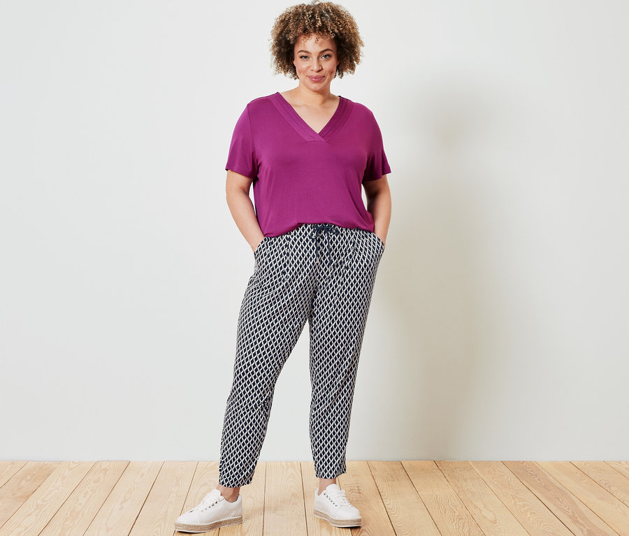Femme posant en T-shirt avec soufflet, baie, et pantalon en jersey imprimé.