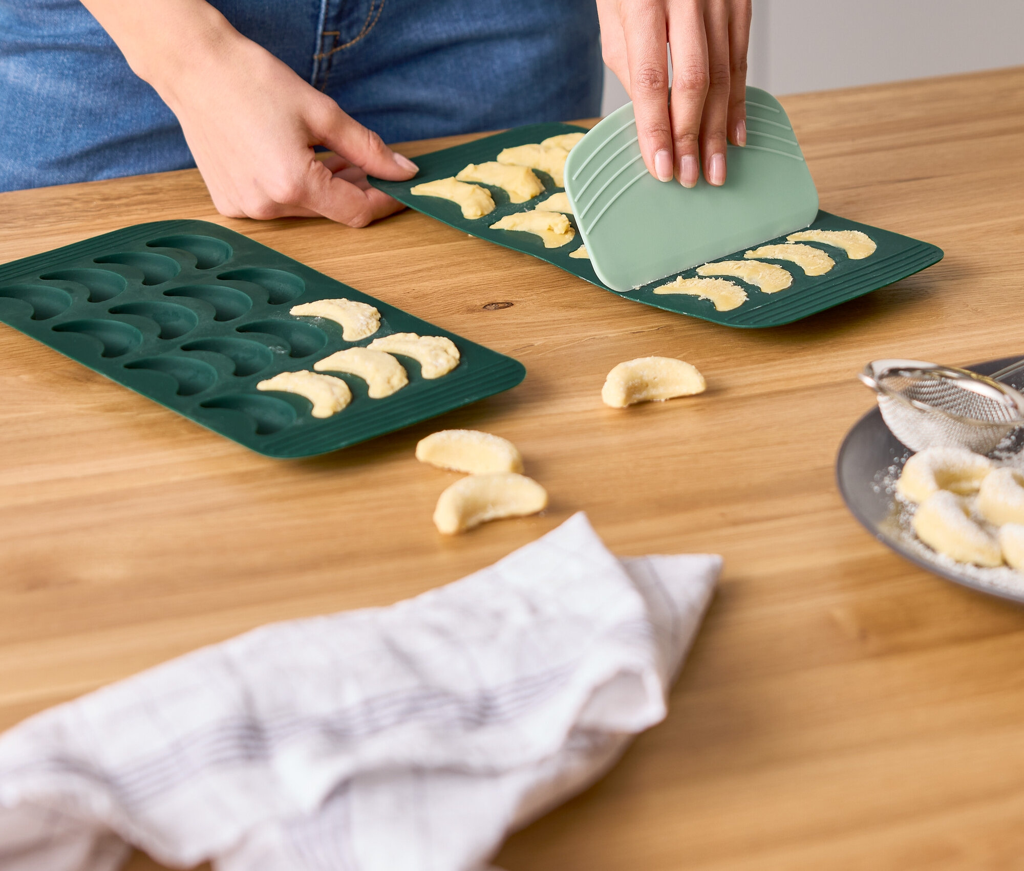 Une femme utilise un grattoir vert pour retirer des biscuits d'un moule à biscuits en forme de croissant.