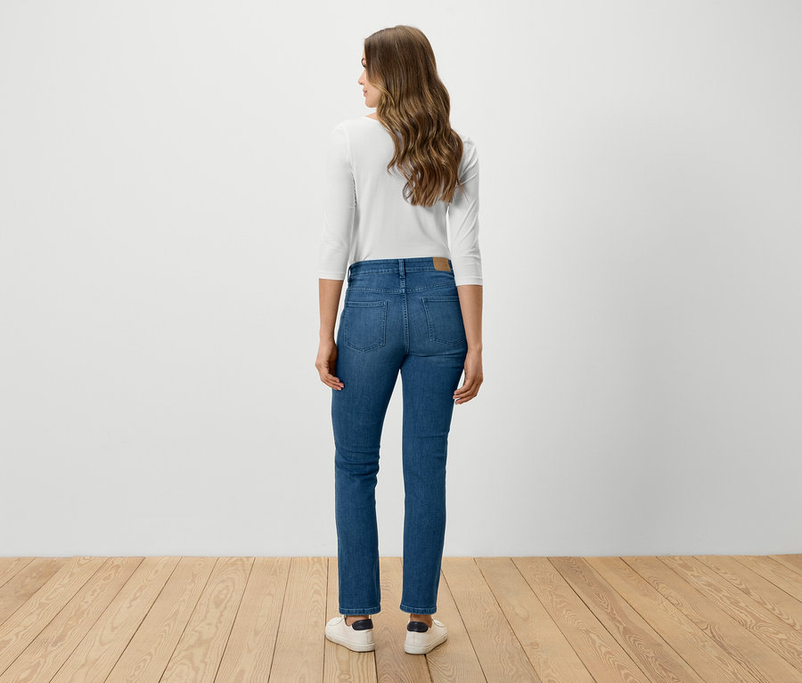 Une femme se tient dos à la caméra et porte un jean bleu, une chemise blanche et des chaussures blanches.