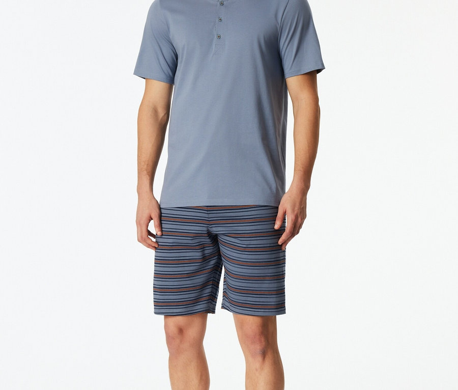 Homme portant un haut de pyjama bleu boutonné et un short rayé.