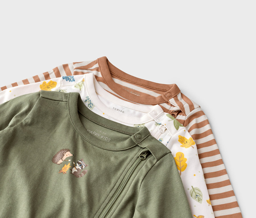 Trois pyjamas pour bébés sont superposés, un vert olive avec un motif animalier, un blanc avec des feuilles et un rayé.