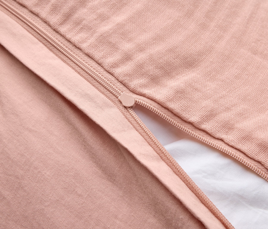 Gros plan d'une housse de couette rose clair partiellement ouverte avec une fermeture éclair sur un drap blanc.