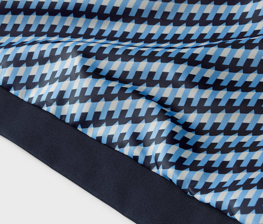 Gros plan d'un tissu à motif géométrique bleu, bleu clair et blanc avec une bordure bleu foncé.