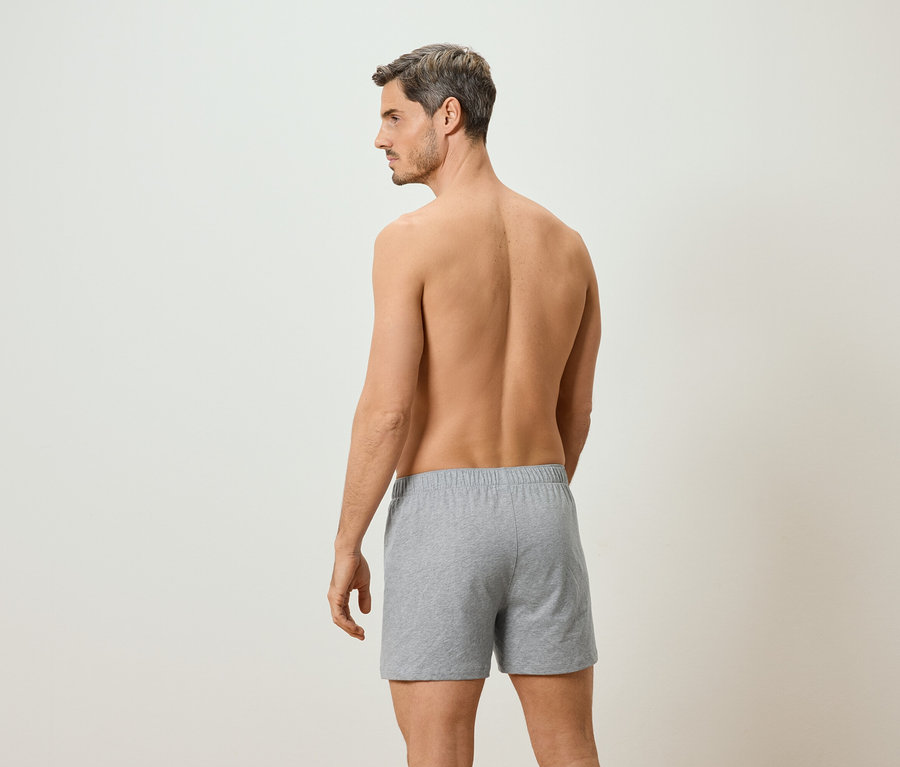 Homme torse nu, vu de dos, portant un boxer gris sur un fond neutre.