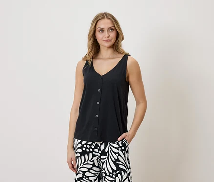 Femme portant un débardeur noir boutonné à col en V et un pantalon à motifs, une main dans la poche.