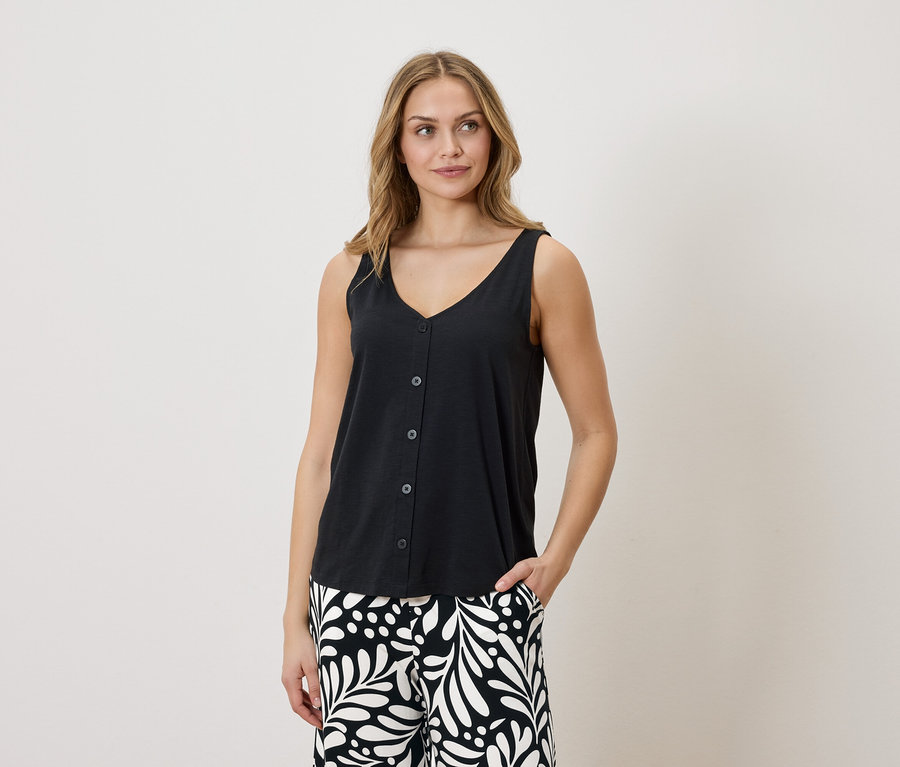 Femme portant un débardeur noir boutonné à col en V et un pantalon à motifs, une main dans la poche.