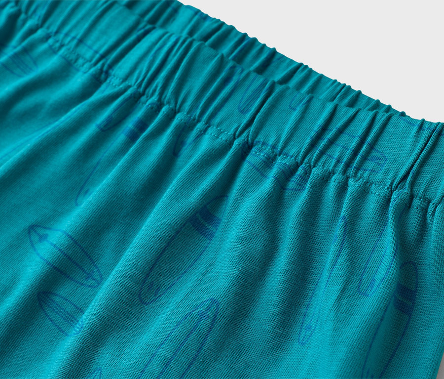 Gros plan d'un short turquoise avec une taille élastique et un motif de planche de surf bleu.