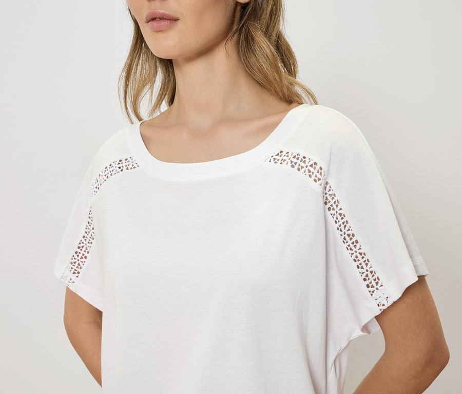Femme portant un t-shirt blanc avec broderie ajourée aux épaules.