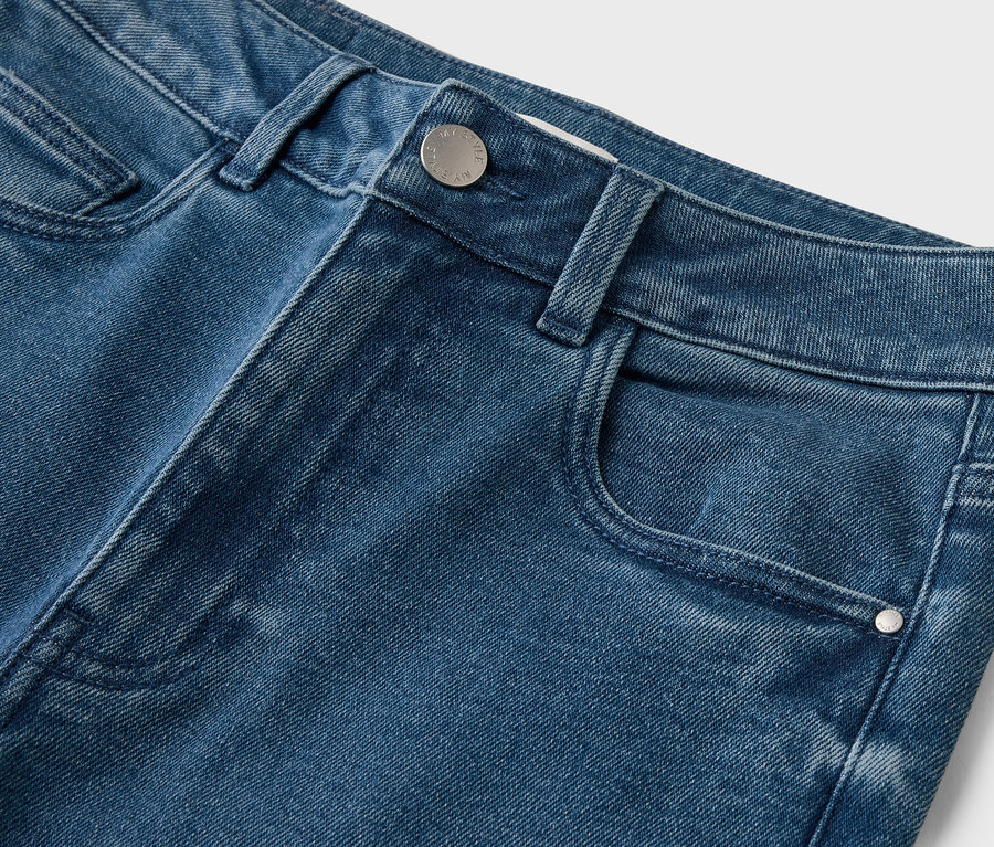 Gros plan d'un jean bleu avec bouton et poche sur fond blanc.