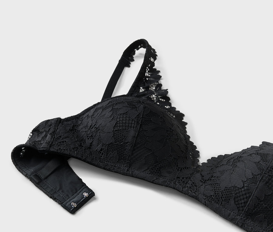 Gros plan d'un soutien-gorge en dentelle noire avec bretelles réglables sur fond gris clair.