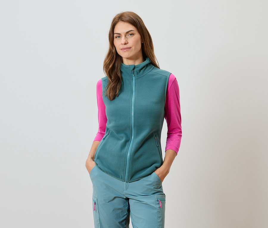 Femme portant un gilet pétrole, un pantalon assorti et un haut rose à manches longues.