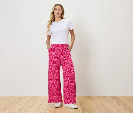 Femme debout avec les mains dans les poches d'un pantalon rose à motifs.