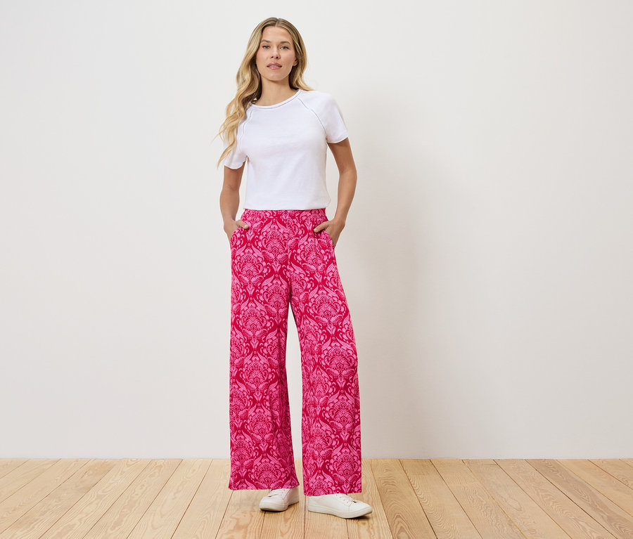 Femme debout avec les mains dans les poches d'un pantalon rose à motifs.