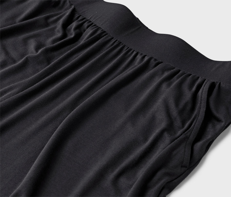 Gros plan d'un pantalon noir avec une taille élastique et des poches sur un fond gris clair.