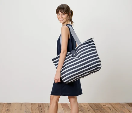 Femme portant une robe bleu marine et un grand sac de transport rayé sur l'épaule.