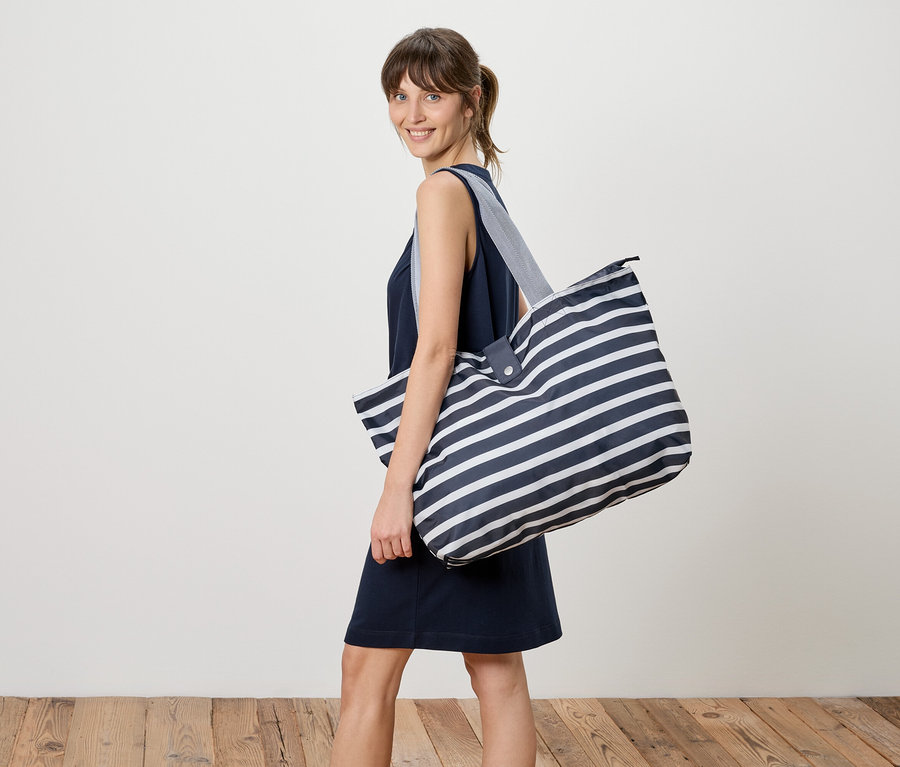 Femme portant une robe bleu marine et un grand sac de transport rayé sur l'épaule.