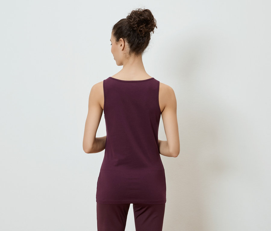 Vue arrière d'une femme portant un débardeur bordeaux et un pantalon, les cheveux relevés en chignon, sur fond blanc.