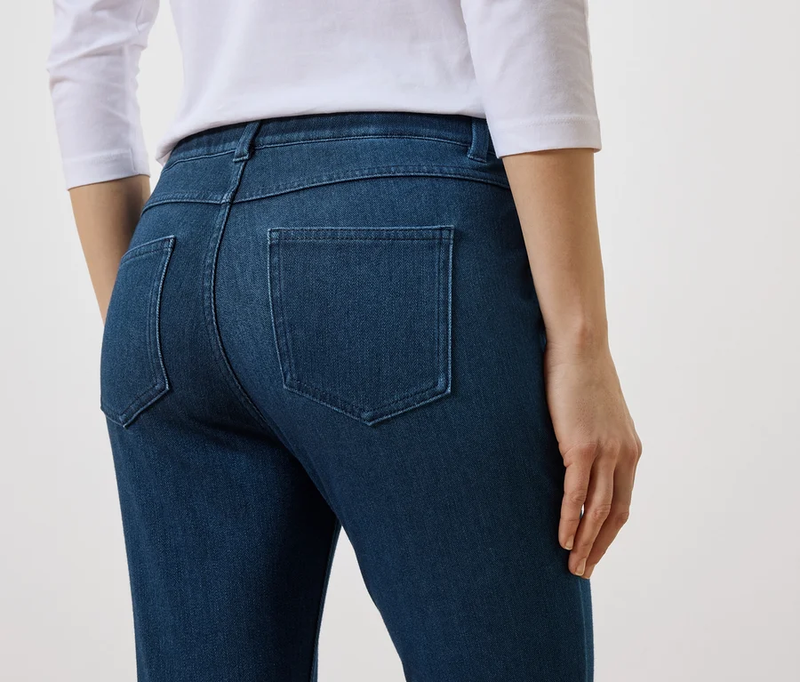 Vue arrière d'une femme portant un haut blanc et un jean bleu avec des poches arrière sur fond blanc.