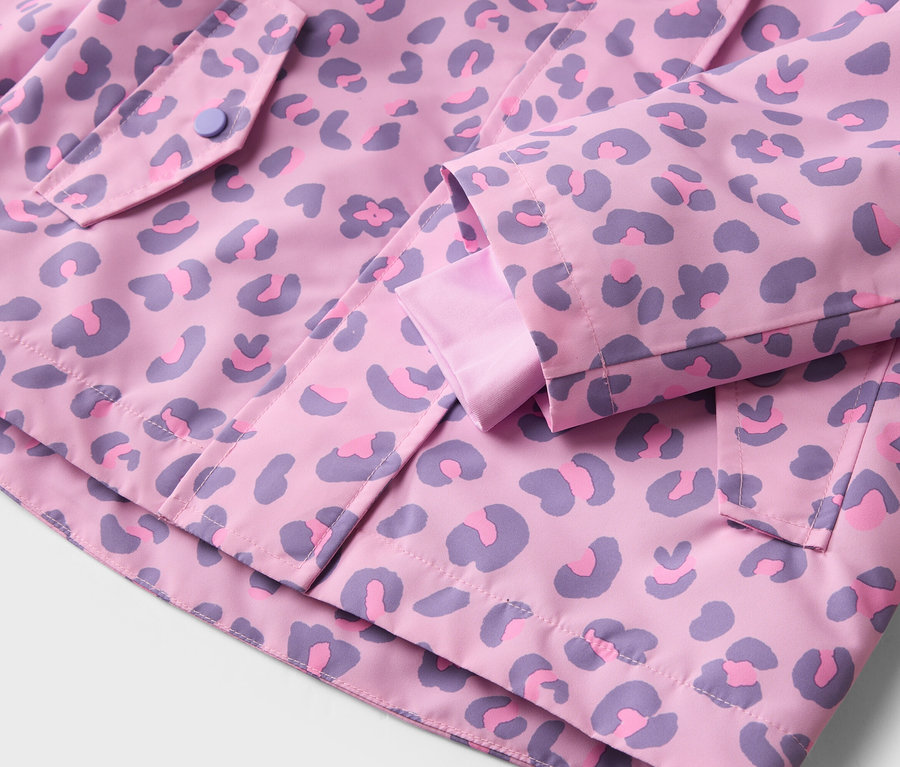 Gros plan sur une veste rose à motif léopard violet, avec un bouton sur la poche et des détails aux manches.