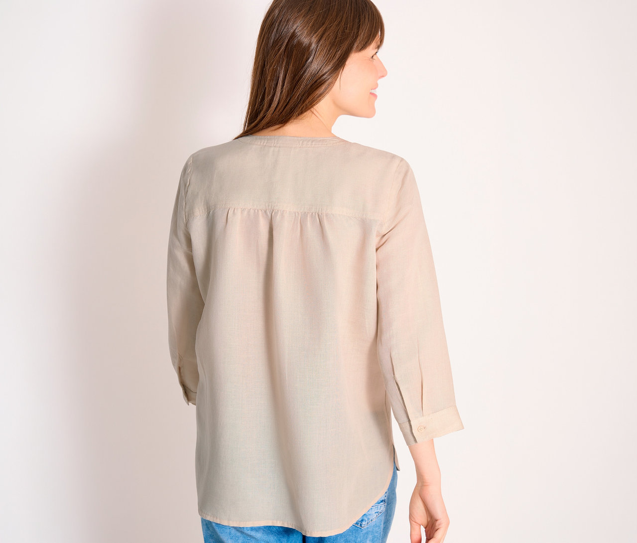 Vue arrière d'une femme aux longs cheveux bruns portant un chemisier beige clair à manches longues et un jean bleu.