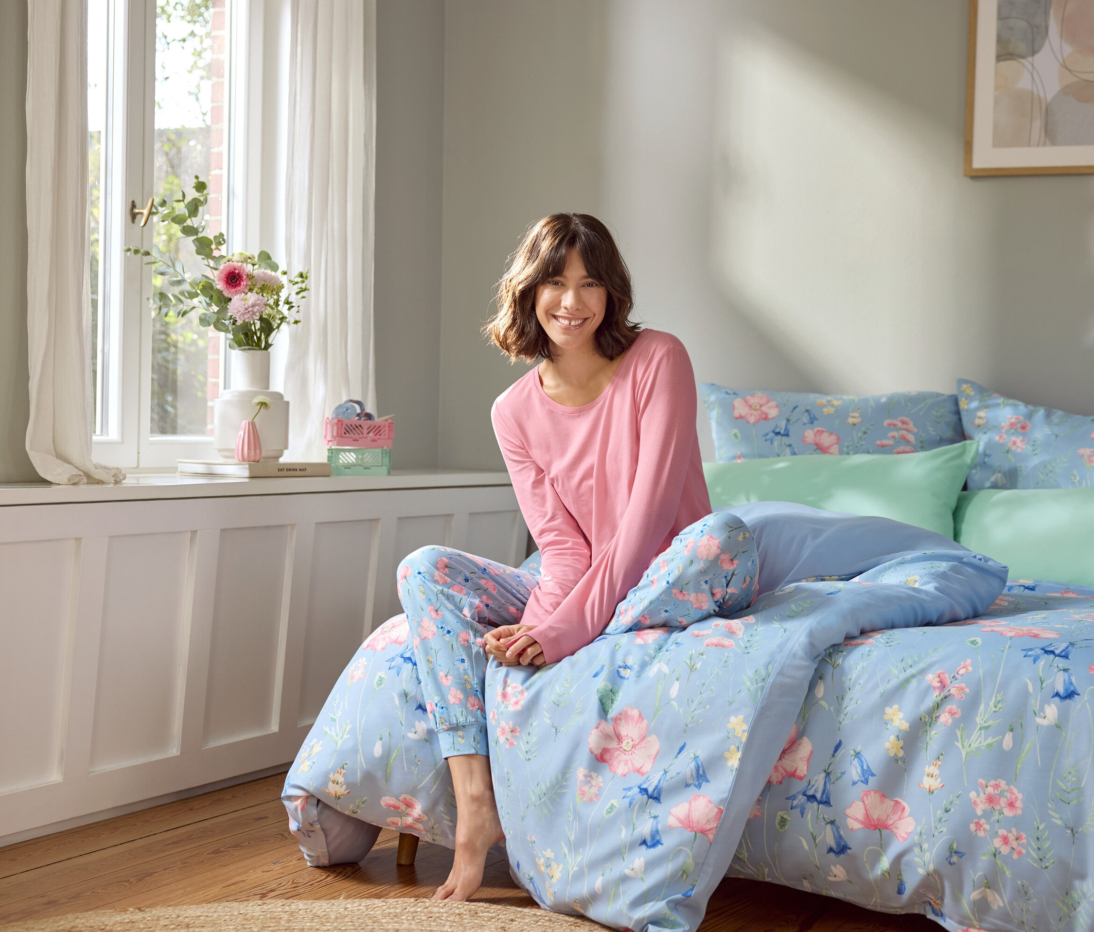 Femme assise sur un lit avec des draps bleu clair à motifs floraux.